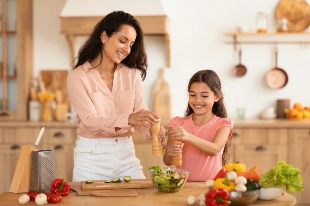 Happy Mother And Preteen Daughter Cooking And Seasoning Salad Indoor