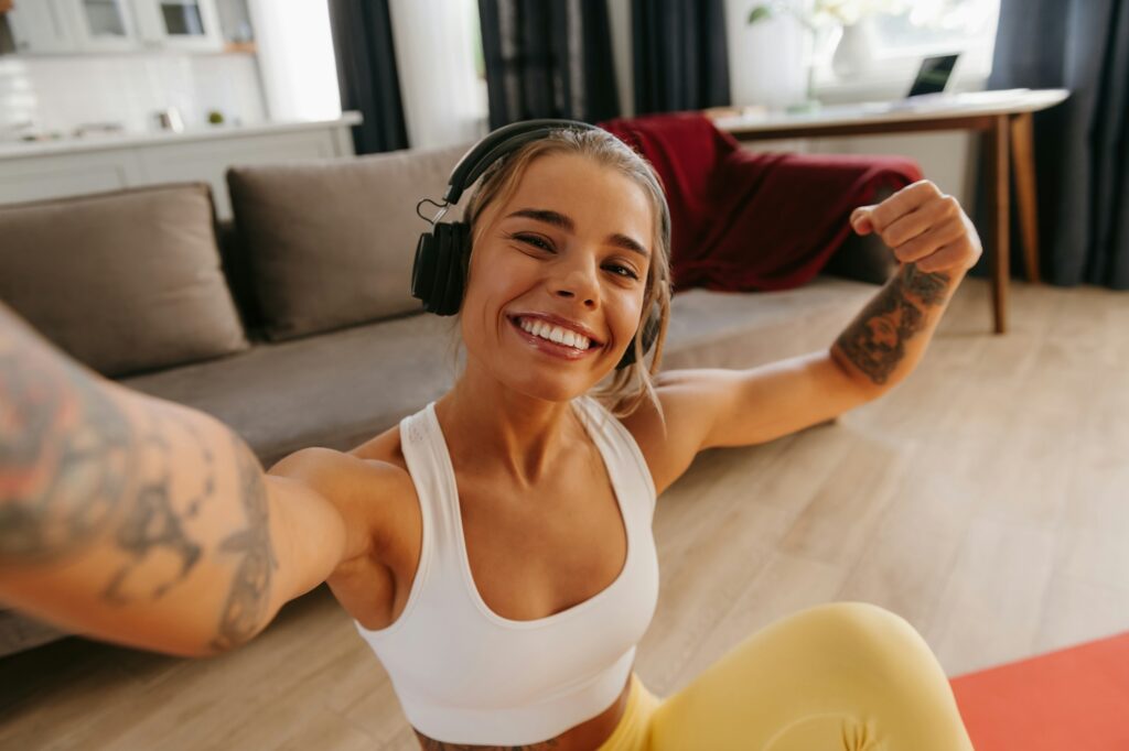 Top view of happy sporty woman making selfie while resting on exercise mat after home workout