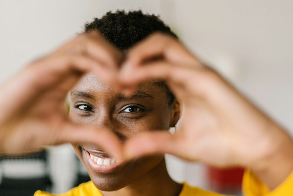 young smiling lovely multiracial woman showing shape heart with hands and looking through it