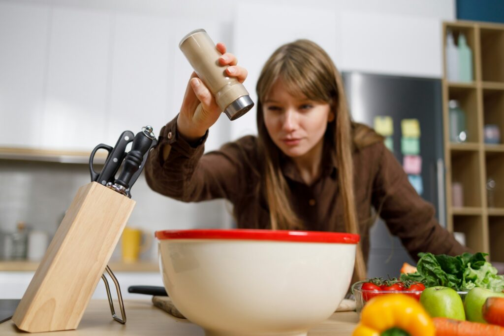 Young woman cooking in the kitchen adding pepper into the bowl