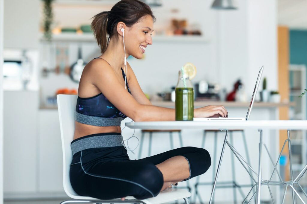 Sporty young woman working with her laptop after session of exercises in the kitchen at home.